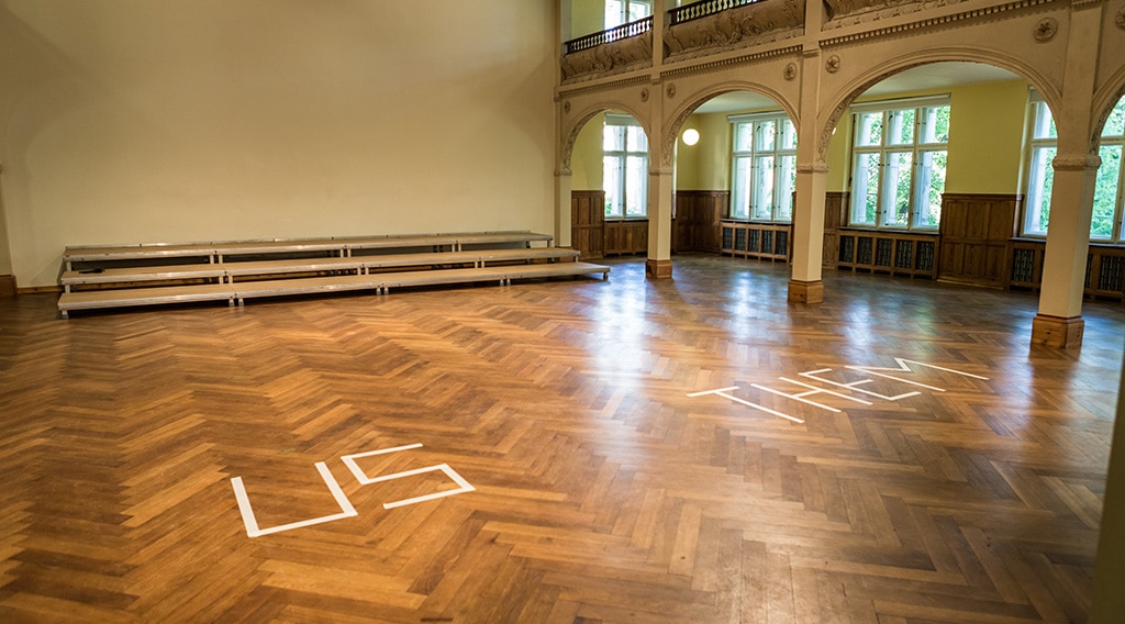 Large room with the words "US" and "THEM" spelled out on the floor with tape.